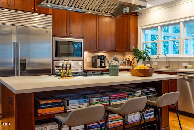 kitchen featuring a sink, range hood, light wood-style floors, light countertops, and built in appliances