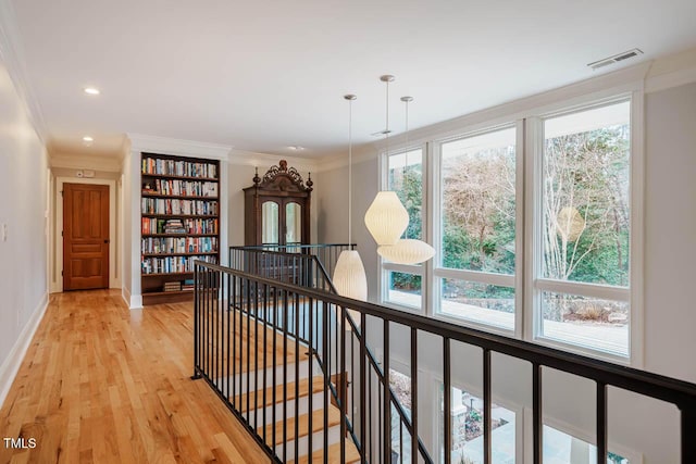 hall featuring baseboards, visible vents, light wood-style flooring, ornamental molding, and an upstairs landing