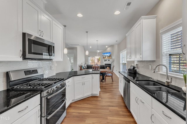 kitchen featuring stainless steel appliances, a sink, white cabinets, open floor plan, and light wood finished floors