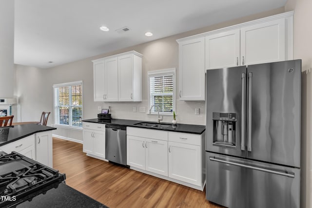 kitchen featuring decorative backsplash, dark countertops, stainless steel appliances, light wood-type flooring, and a sink