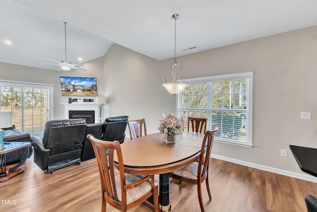 dining space featuring light wood finished floors, baseboards, visible vents, vaulted ceiling, and a fireplace