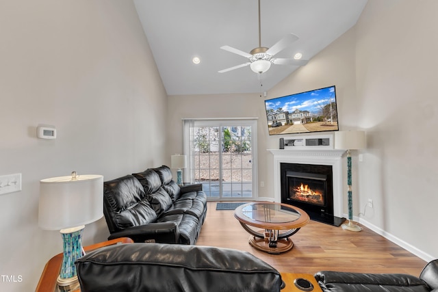 living area with baseboards, a ceiling fan, a glass covered fireplace, wood finished floors, and high vaulted ceiling