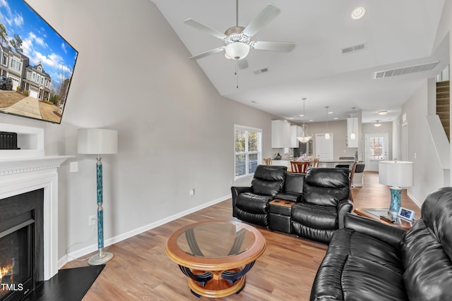 living area with a lit fireplace, light wood finished floors, visible vents, and baseboards