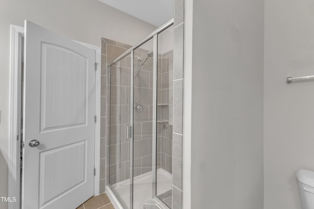 full bath featuring toilet, a stall shower, and tile patterned flooring