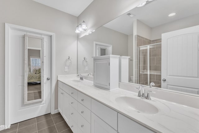 ensuite bathroom with double vanity, a shower stall, a sink, and tile patterned floors