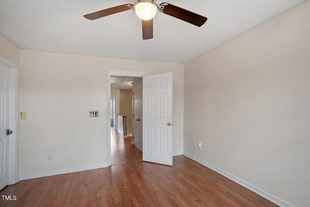 unfurnished room with a textured ceiling, wood finished floors, and baseboards