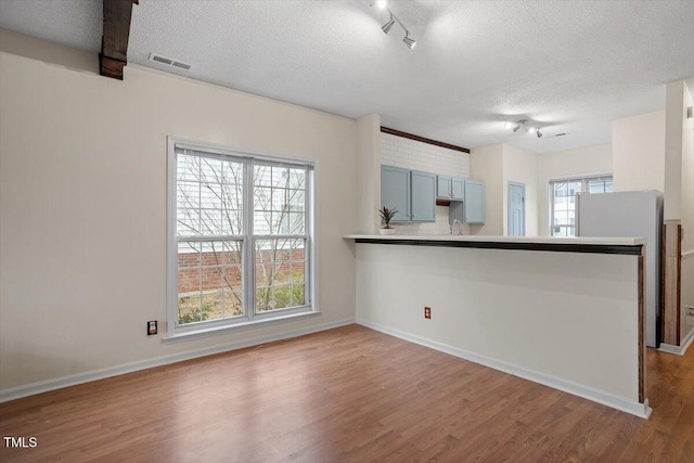 kitchen featuring a textured ceiling, a peninsula, wood finished floors, visible vents, and freestanding refrigerator