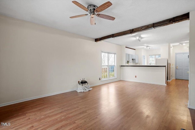 unfurnished living room with baseboards, ceiling fan, a textured ceiling, light wood-type flooring, and beam ceiling