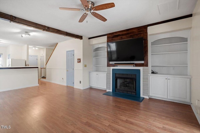 unfurnished living room with a large fireplace, visible vents, beamed ceiling, and wood finished floors