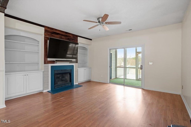 unfurnished living room with a large fireplace, a ceiling fan, light wood-style flooring, and built in features