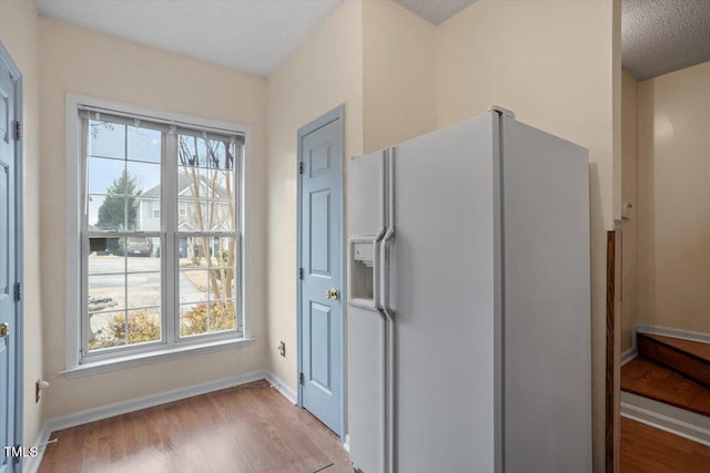 kitchen featuring white refrigerator with ice dispenser, light wood-style flooring, baseboards, and a textured ceiling