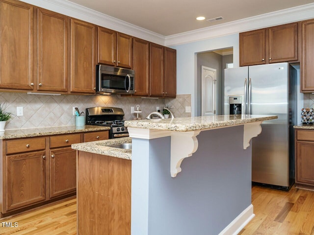 kitchen featuring crown molding, a center island with sink, light wood-type flooring, and stainless steel appliances