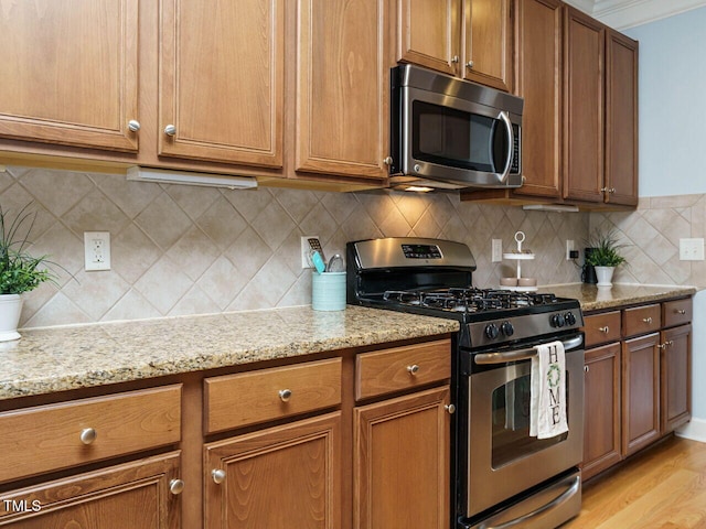 kitchen with brown cabinetry, tasteful backsplash, light stone countertops, and stainless steel appliances