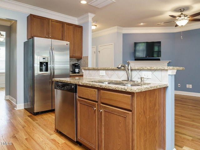 kitchen with a sink, light stone counters, appliances with stainless steel finishes, and crown molding