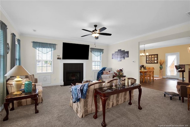 living area featuring carpet, crown molding, a tile fireplace, baseboards, and ceiling fan with notable chandelier