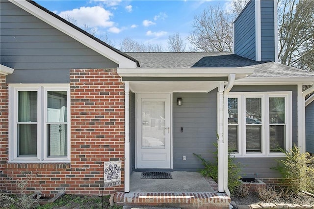 doorway to property featuring a shingled roof and brick siding