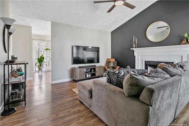 living room with ceiling fan, a fireplace, wood finished floors, baseboards, and vaulted ceiling