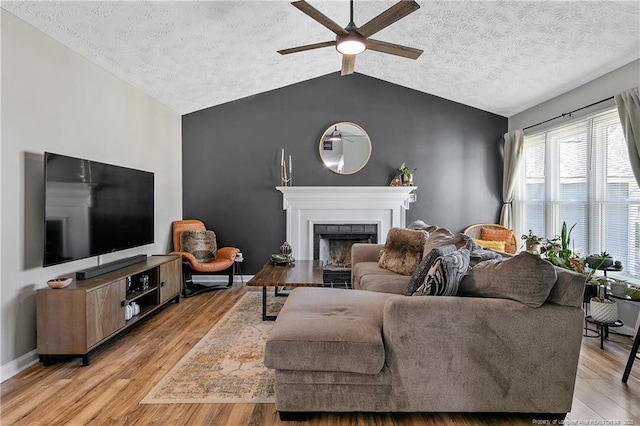 living room featuring a ceiling fan, vaulted ceiling, a textured ceiling, light wood-type flooring, and a fireplace