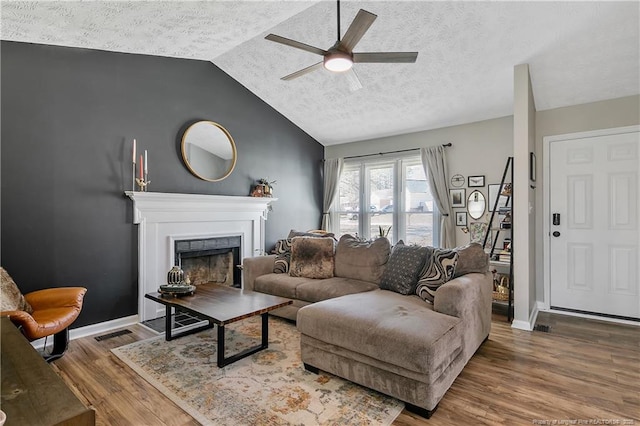 living area featuring lofted ceiling, a fireplace, baseboards, and wood finished floors