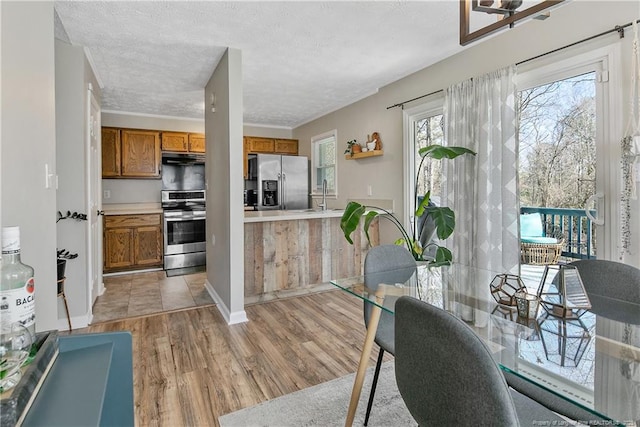 kitchen featuring stainless steel appliances, brown cabinetry, light countertops, and light wood-style flooring