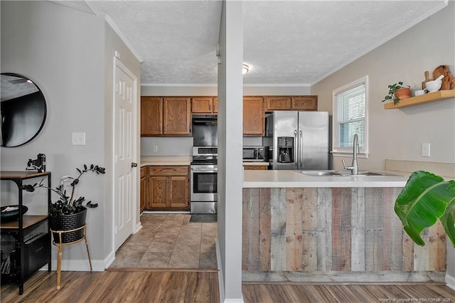 kitchen featuring brown cabinetry, a peninsula, stainless steel appliances, light countertops, and a sink