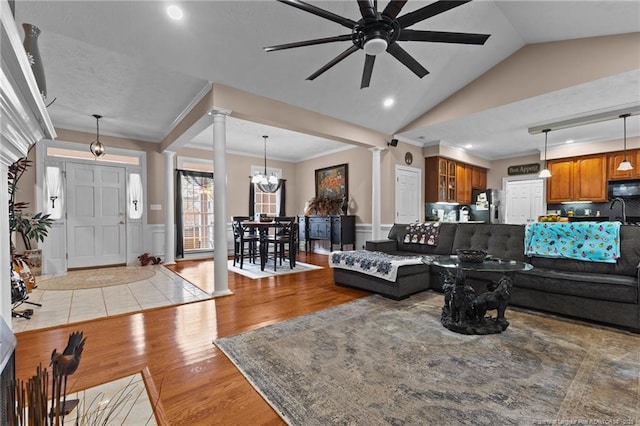 living area featuring ornate columns, vaulted ceiling, light wood finished floors, and a wainscoted wall