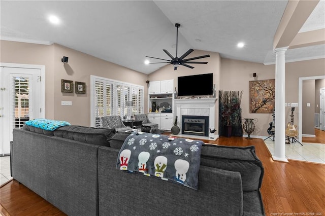 living room with decorative columns, a tiled fireplace, lofted ceiling, ceiling fan, and wood finished floors