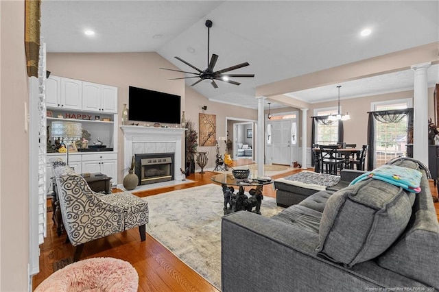 living room featuring decorative columns, lofted ceiling, wood finished floors, a tile fireplace, and ceiling fan with notable chandelier