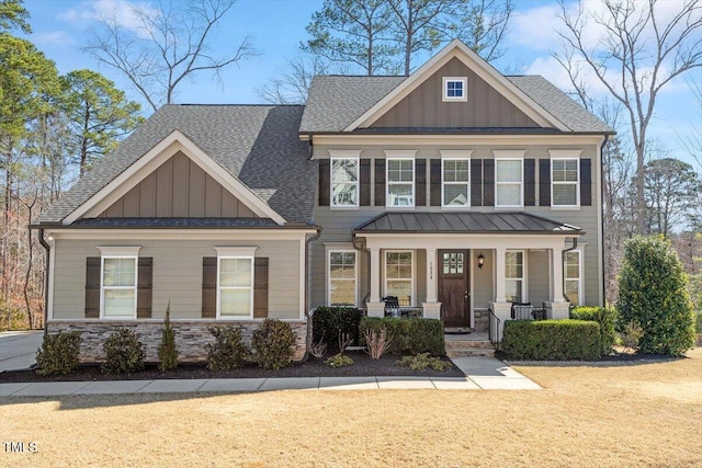 craftsman-style house with stone siding, a porch, board and batten siding, a front yard, and a shingled roof