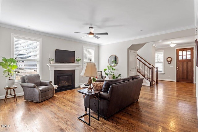 living area with a glass covered fireplace, wood finished floors, stairway, and a ceiling fan