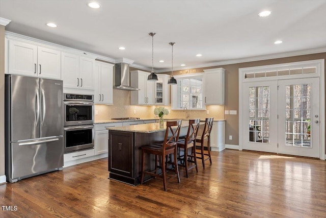 kitchen with decorative backsplash, appliances with stainless steel finishes, dark wood-style floors, wall chimney exhaust hood, and a sink