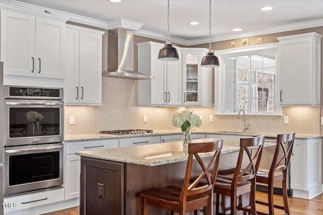 kitchen with a kitchen island, appliances with stainless steel finishes, a kitchen bar, crown molding, and wall chimney range hood