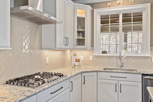 kitchen featuring glass insert cabinets, stainless steel appliances, white cabinetry, wall chimney exhaust hood, and a sink