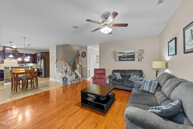 living room featuring stairway, a ceiling fan, visible vents, baseboards, and light wood-type flooring