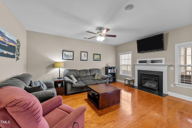 living room featuring baseboards, plenty of natural light, a glass covered fireplace, and light wood finished floors