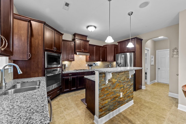 kitchen featuring tasteful backsplash, under cabinet range hood, appliances with stainless steel finishes, arched walkways, and a sink