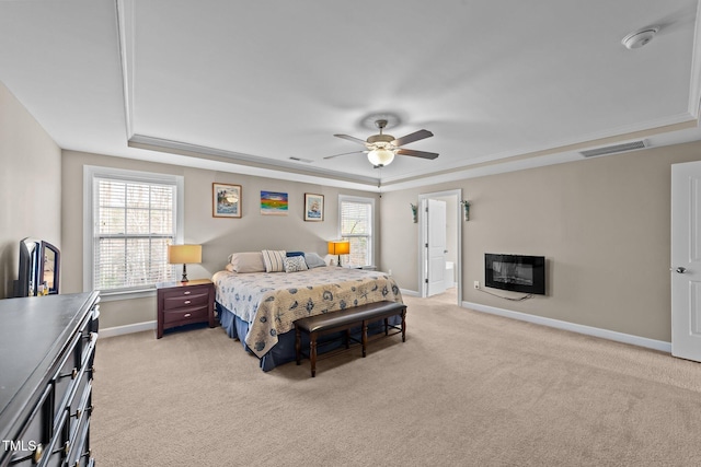 bedroom featuring visible vents, a glass covered fireplace, baseboards, a raised ceiling, and light colored carpet