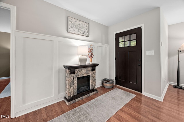 foyer entrance with wood finished floors, baseboards, a fireplace, wainscoting, and a decorative wall