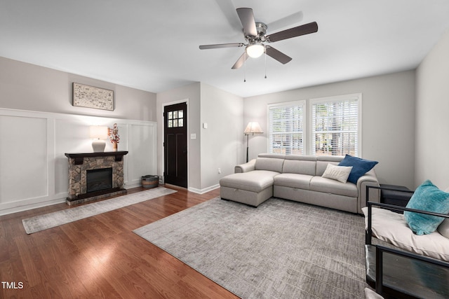 living area with ceiling fan, a stone fireplace, wood finished floors, and a decorative wall