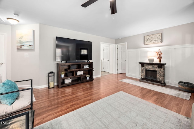 living area featuring a fireplace, a decorative wall, wood finished floors, and a ceiling fan