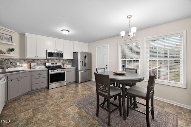 kitchen featuring gray cabinetry, a sink, appliances with stainless steel finishes, a notable chandelier, and tasteful backsplash