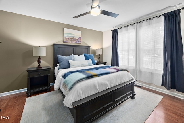 bedroom with a ceiling fan, wood finished floors, visible vents, and baseboards