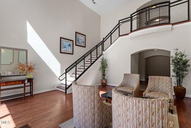 sitting room featuring baseboards, arched walkways, wood finished floors, and a towering ceiling