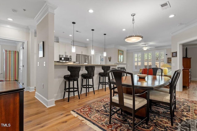 dining space featuring baseboards, visible vents, light wood-style flooring, ceiling fan, and crown molding