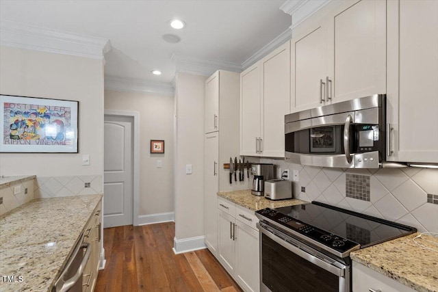 kitchen featuring ornamental molding, wood finished floors, white cabinetry, appliances with stainless steel finishes, and baseboards