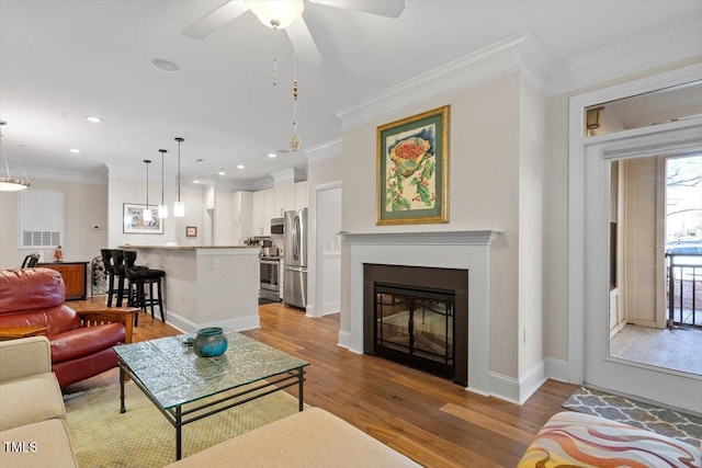 living area featuring light wood-style flooring, recessed lighting, ceiling fan, ornamental molding, and a glass covered fireplace