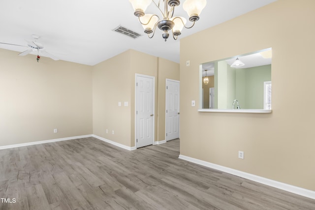 unfurnished room featuring visible vents, a sink, wood finished floors, baseboards, and ceiling fan with notable chandelier