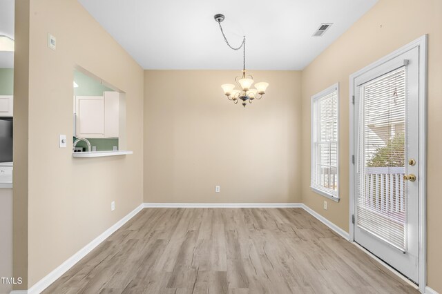 unfurnished dining area featuring baseboards, light wood-style flooring, visible vents, and an inviting chandelier