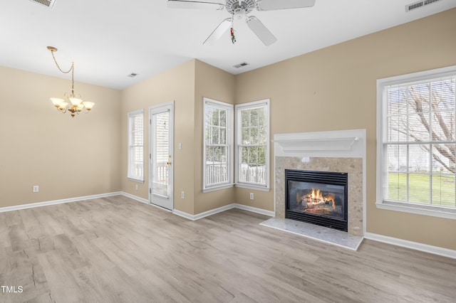 unfurnished living room with visible vents, baseboards, a premium fireplace, wood finished floors, and ceiling fan with notable chandelier