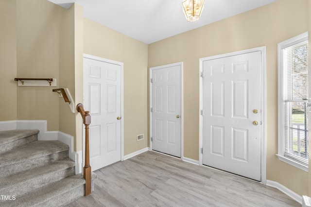 foyer entrance with plenty of natural light, stairway, light wood-style flooring, and baseboards